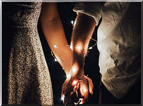 Two people holding hands with a light garland wrapped around their arm